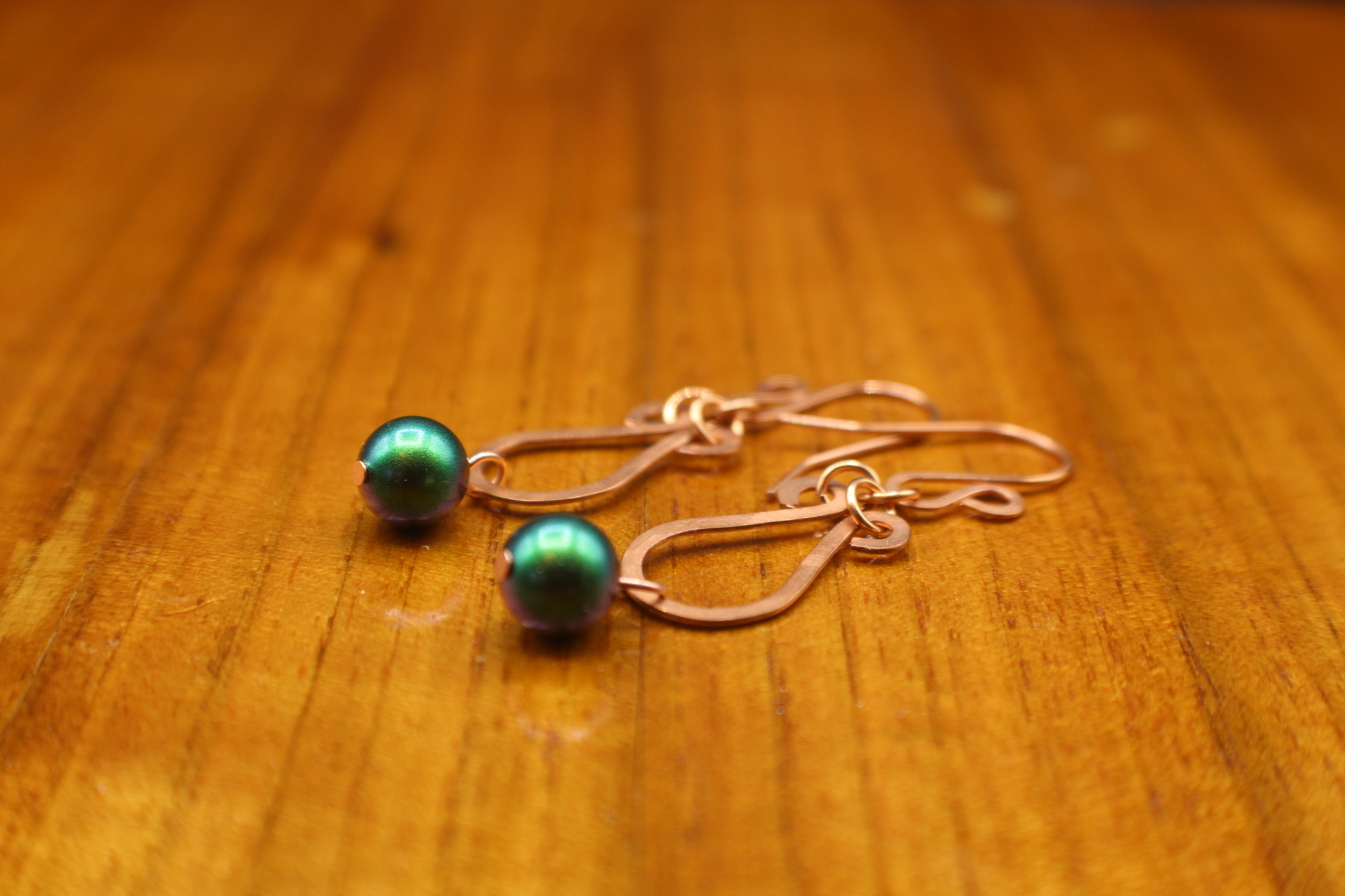 Pair of hammered copper teardrop earrings with green beads on a wooden surface