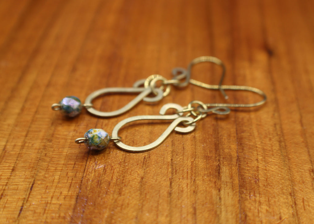 Hammered brass teardrop earrings with mottled yellow/blue bead drops on a wooden surface