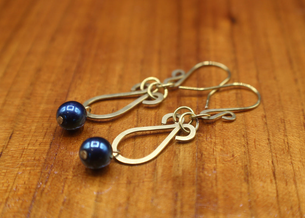 Hammered brass teardrop earrings with metallic dark teal bead drops on a wooden surface