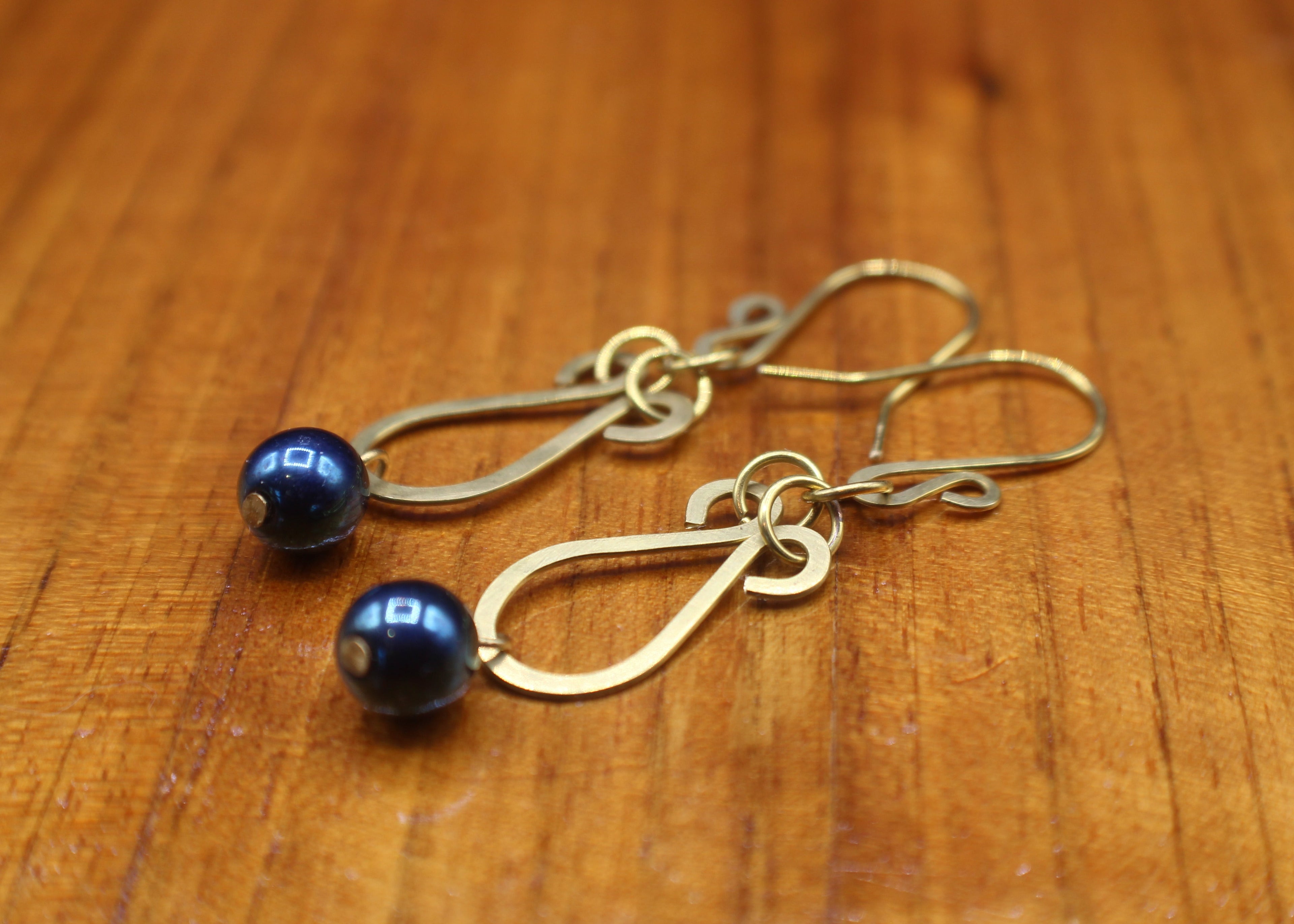 Hammered brass teardrop earrings with metallic dark teal bead drops on a wooden surface