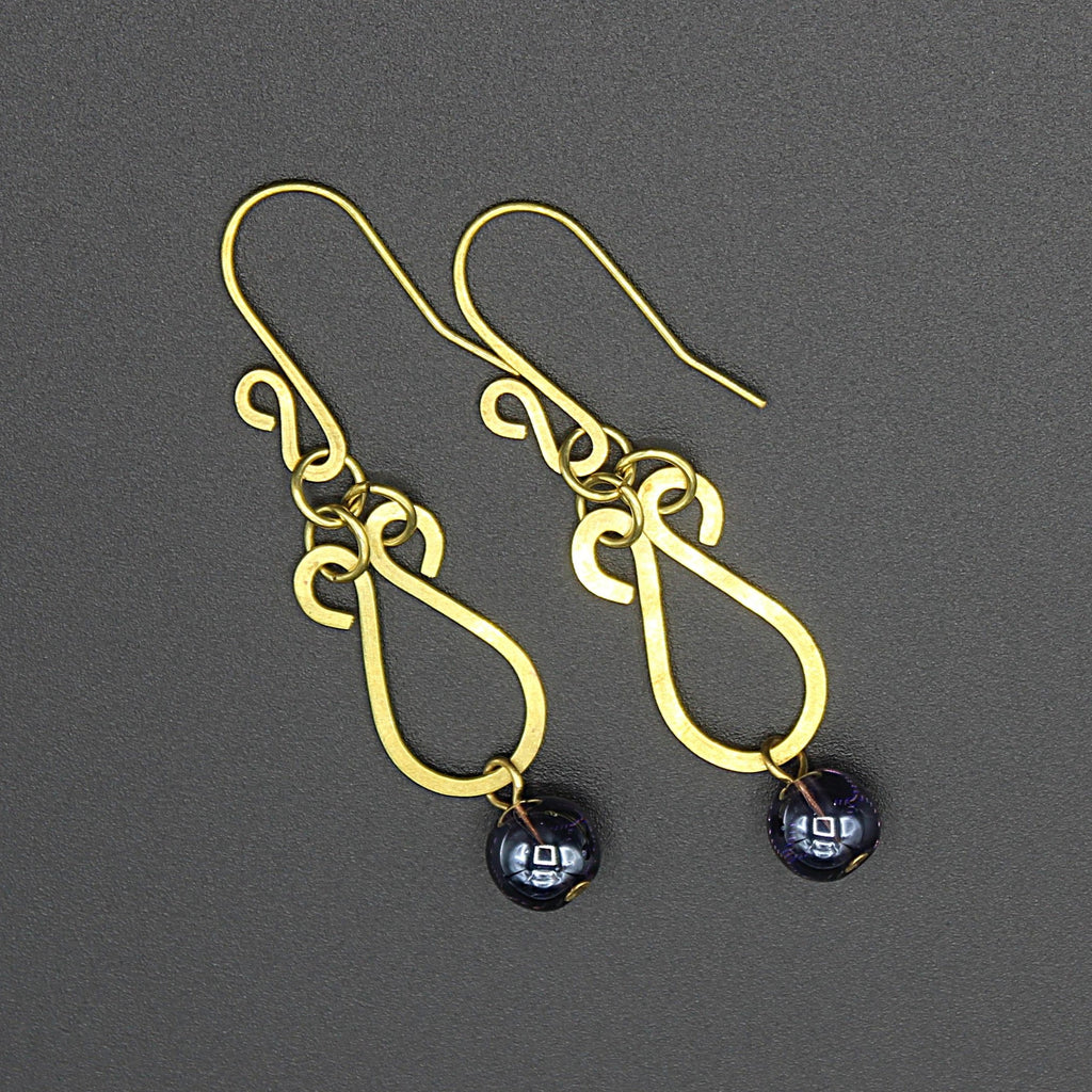 Hammered brass teardrop earrings with dark purple bead drops on a gray background.