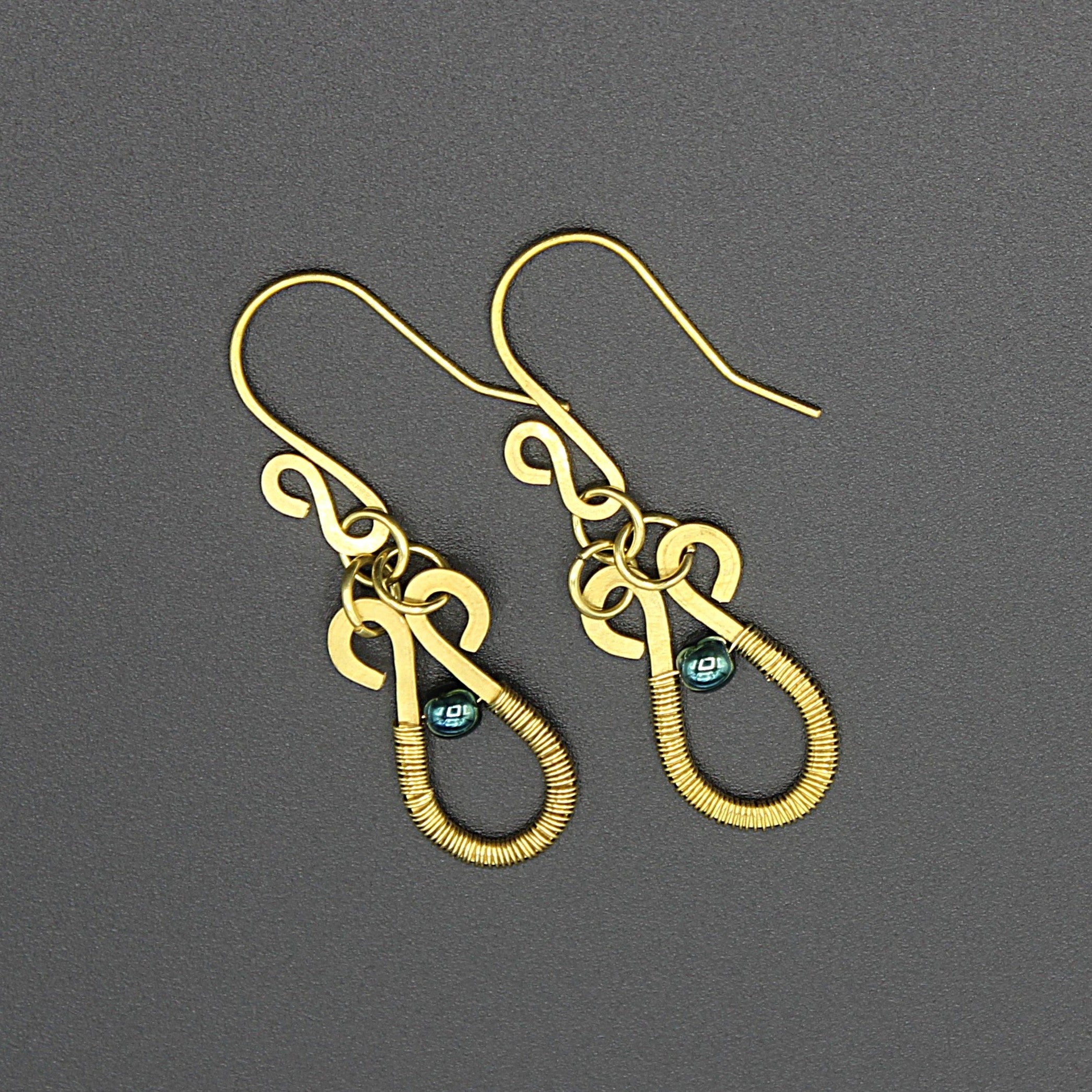 Hammered brass teardrop earrings wire-wrapped with metallic teal bead accents on a gray background.