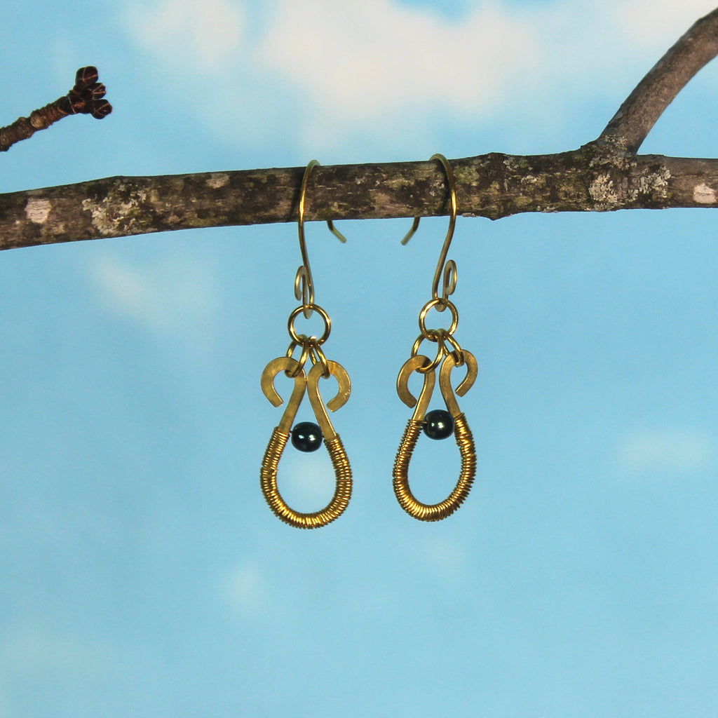 Hammered brass teardrop earrings wire-wrapped with metallic teal bead accents hanging from a branch against a blue sky.