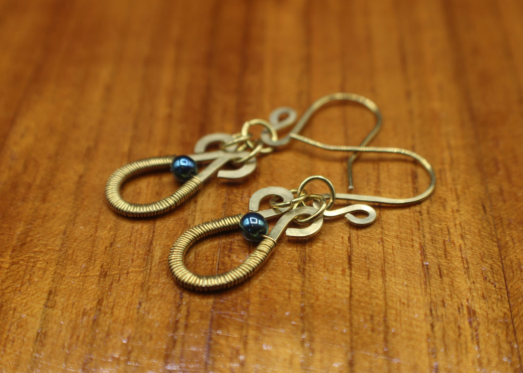 Hammered brass teardrop earrings wire-wrapped with metallic teal bead accents on a wooden surface