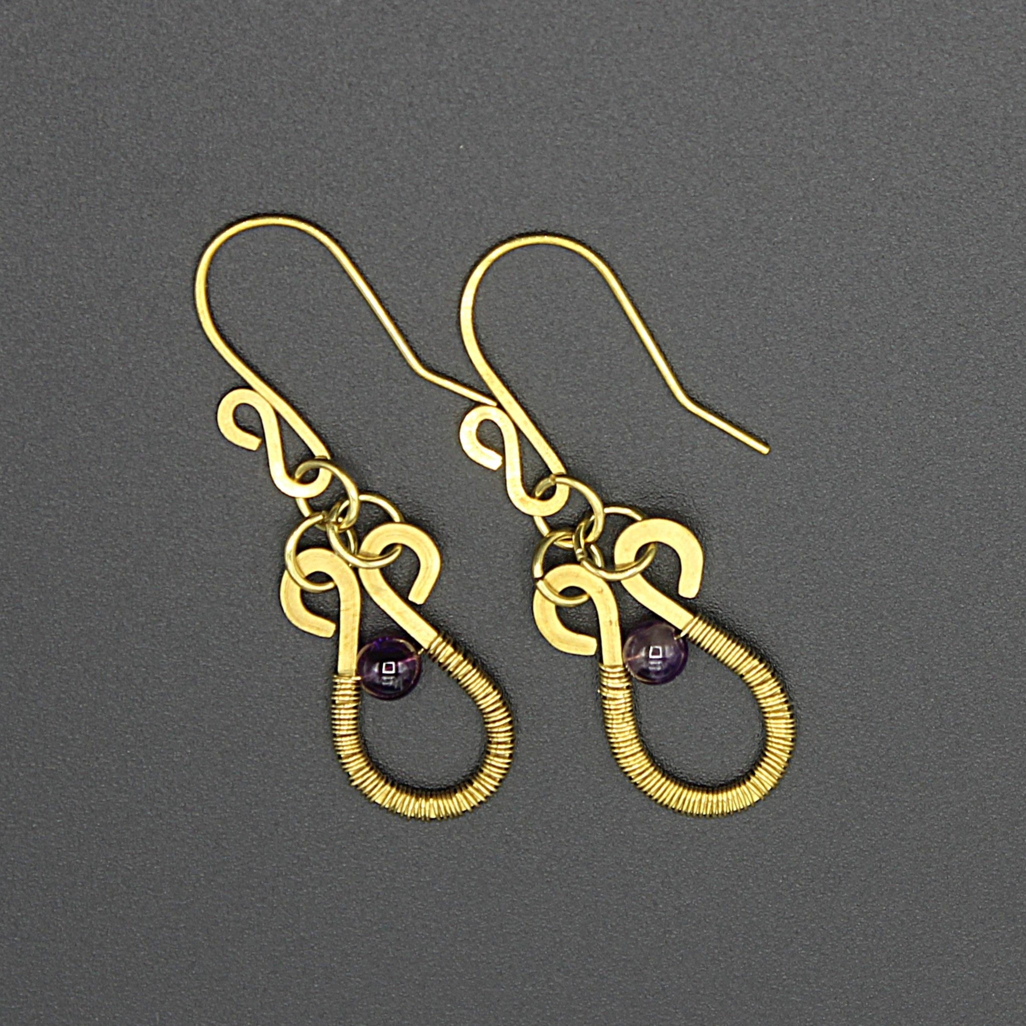 Brass hammered wire earrings with purple amethyst beads and wire wrapping on a gray background