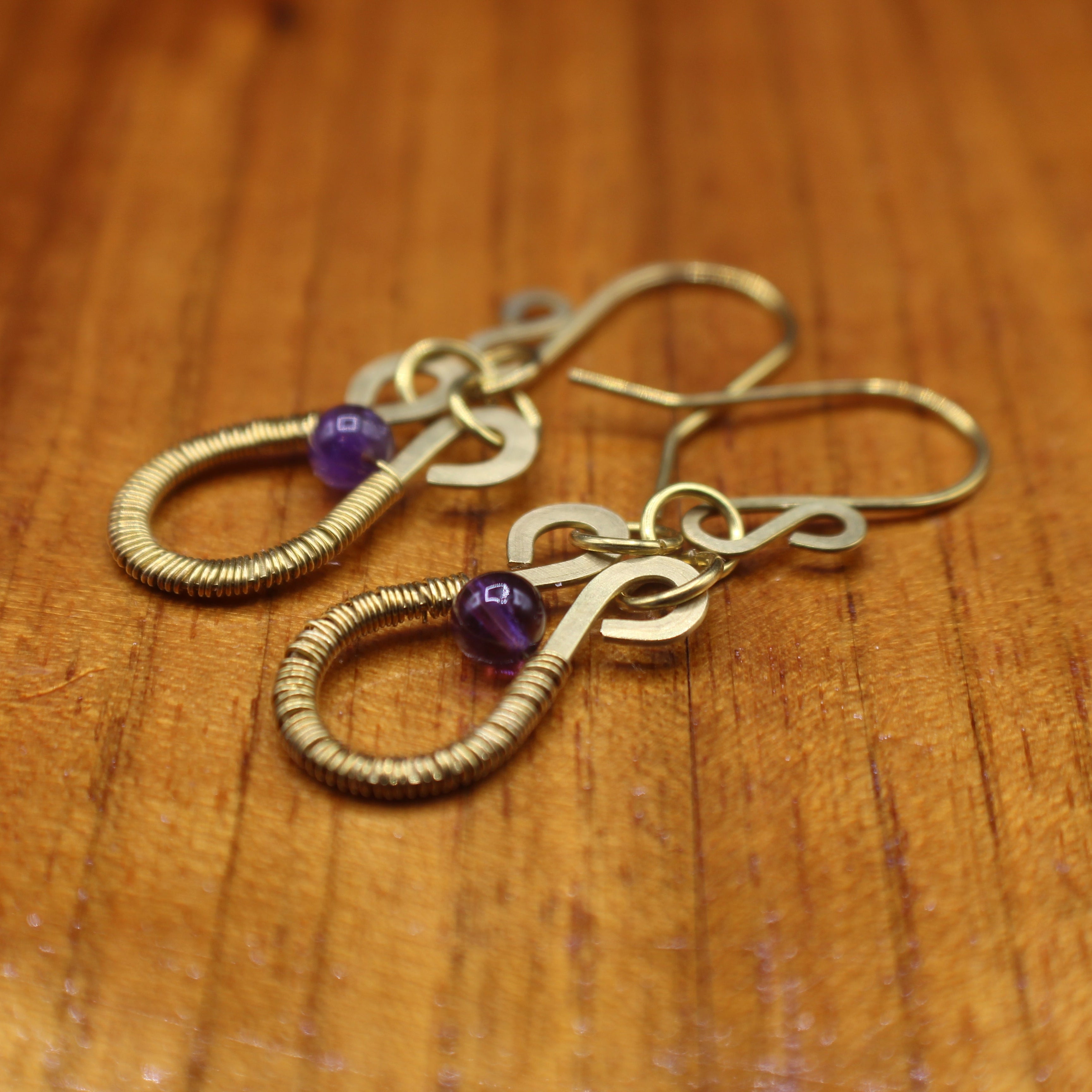 Hammered brass wire earrings with purple amethyst beads and wire wrapping on a wooden surface