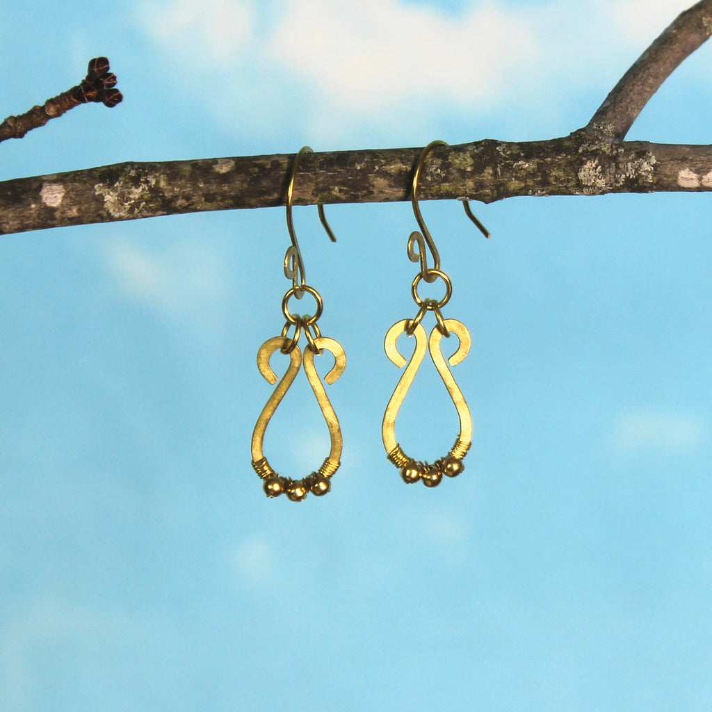 Hammered brass teardrop earrings with small brass bead accents hanging from a branch against a blue sky background