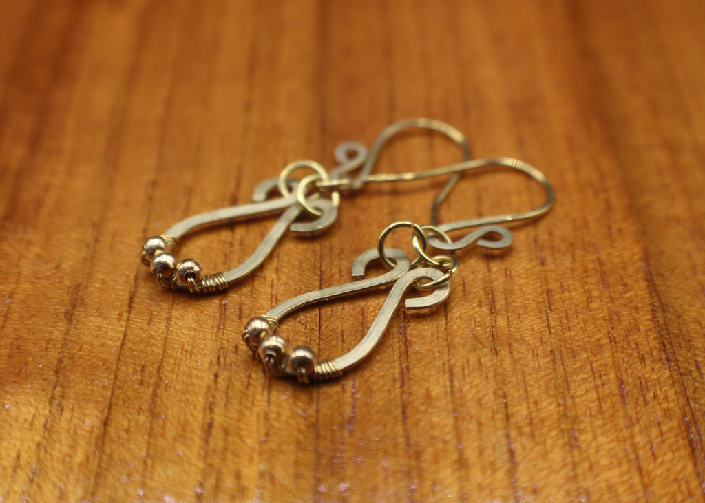 Hammered brass teardrop earrings with small brass bead accents on a wooden surface