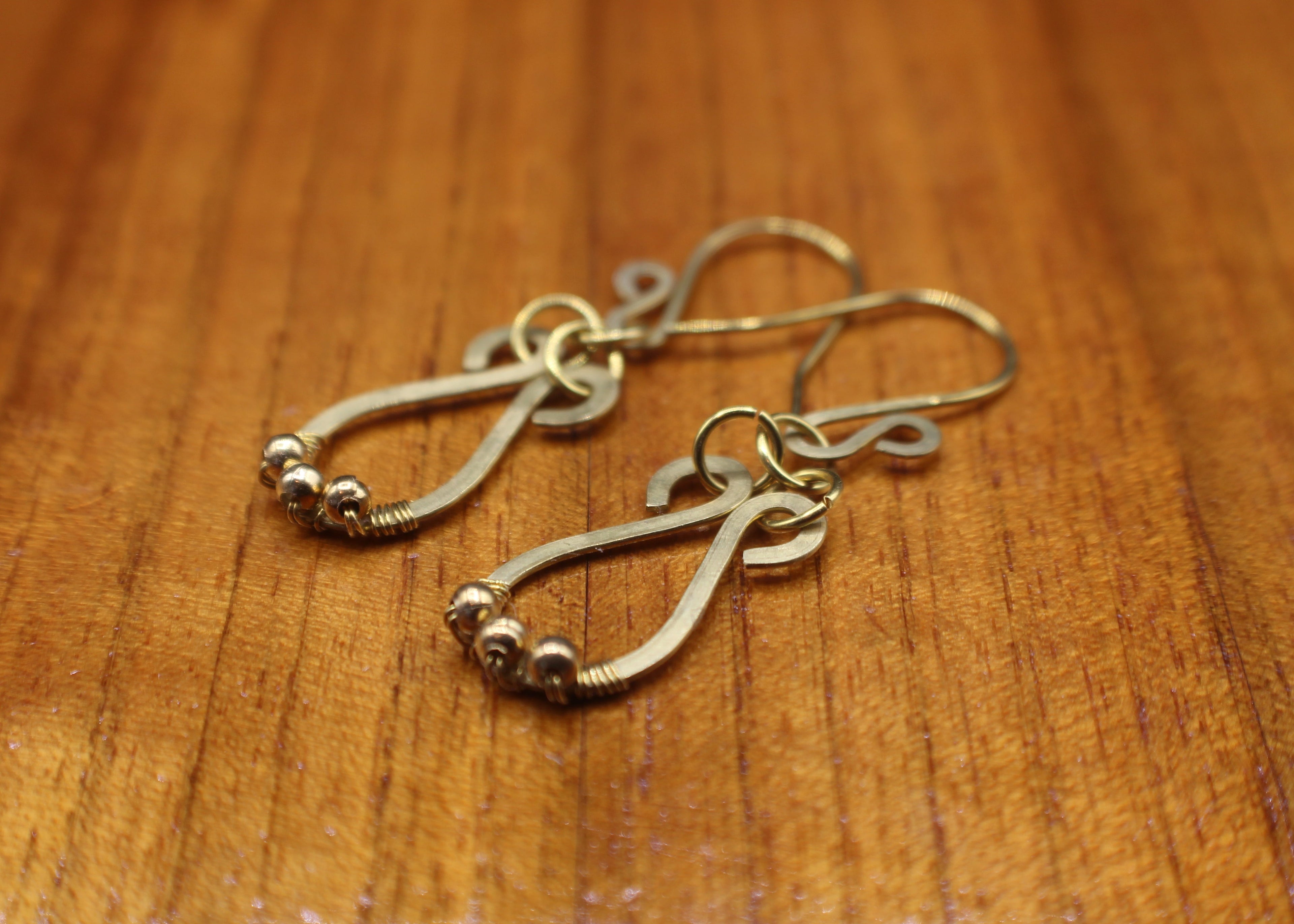Hammered brass teardrop earrings with small brass bead accents on a wooden surface