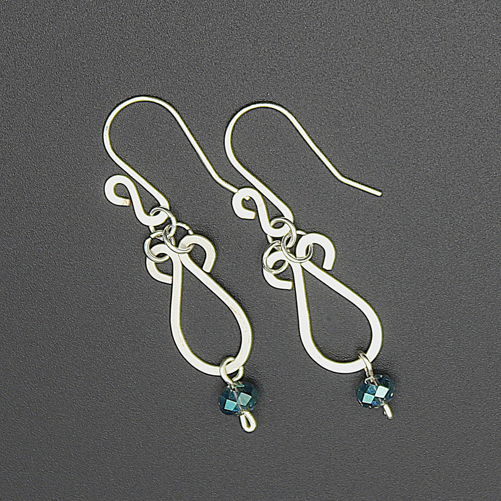 Hammered silver teardrop earrings with faceted blue bead drops on a gray background.