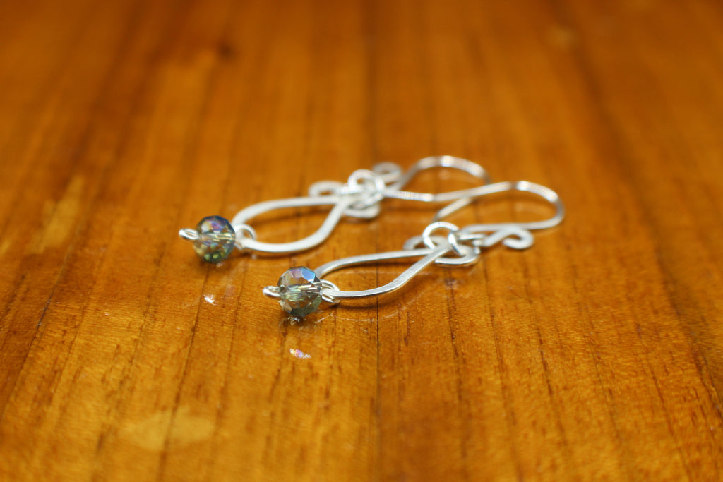 Hammered silver teardrop earrings with faceted blue bead drops on a wooden surface