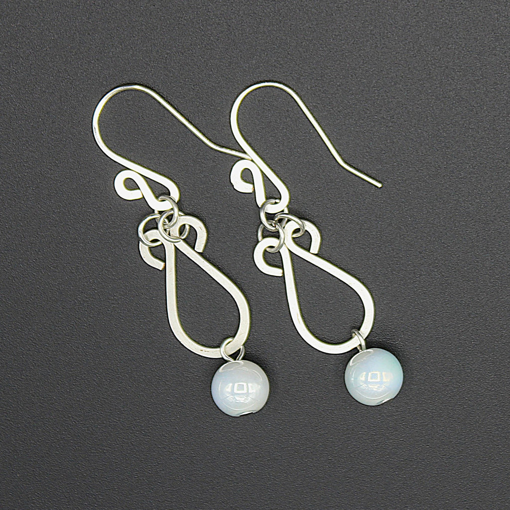 Hammered silver earrings with pale blue bead drops on a gray background.