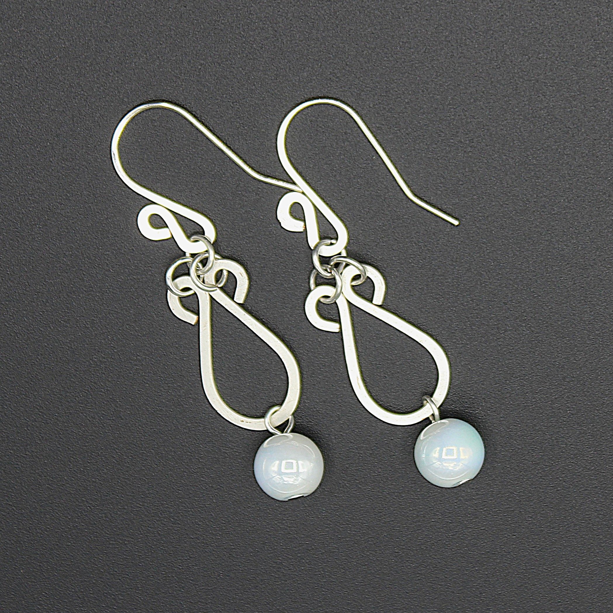 Hammered silver earrings with pale blue bead drops on a gray background.