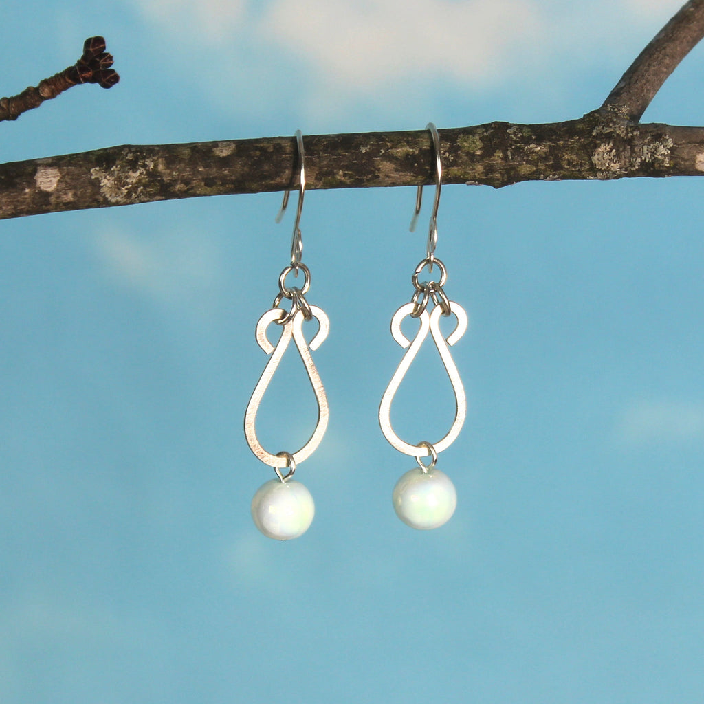 Hammered silver earrings with pale blue bead drops hanging from a branch against a blue sky background