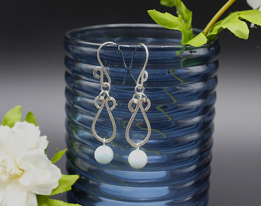 Hammered silver earrings with pale blue bead drops hanging on a blue vase.