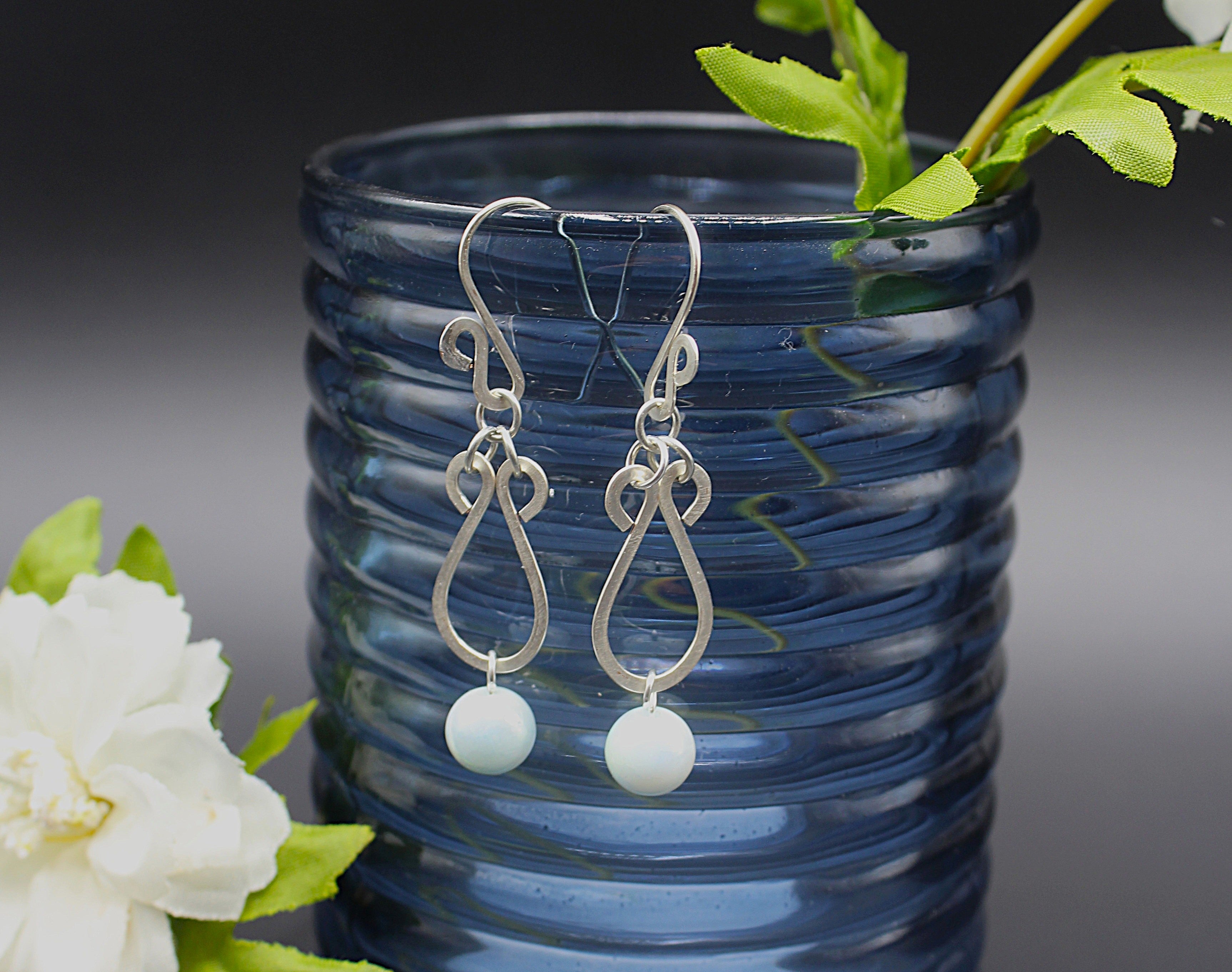 Hammered silver earrings with pale blue bead drops hanging on a blue vase.