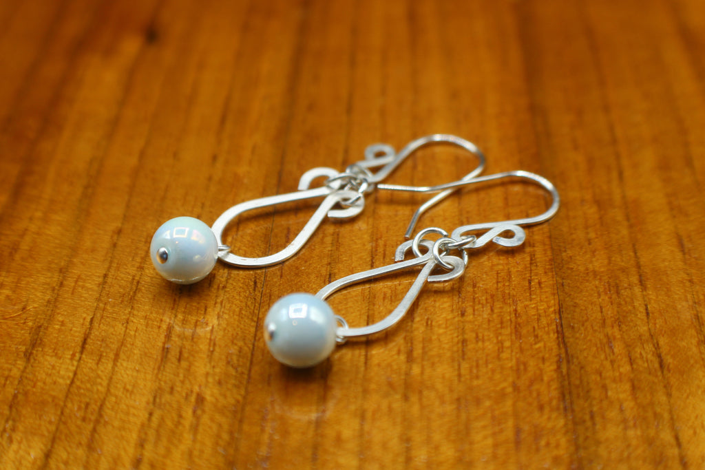 Hammered silver earrings with pale blue bead drops on a wooden surface