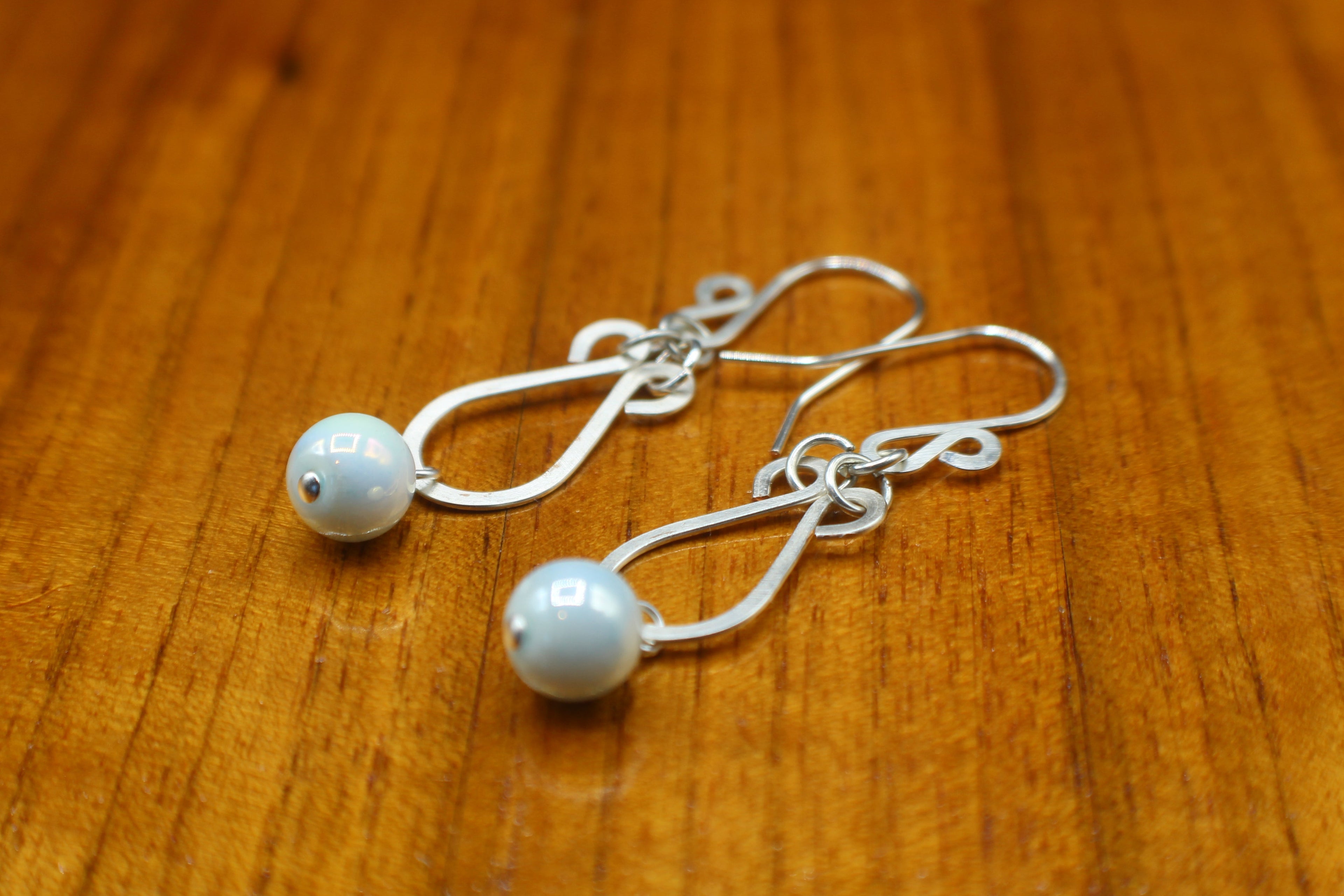 Hammered silver earrings with pale blue bead drops on a wooden surface