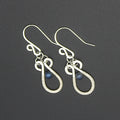 Hammered silver teardrop earrings with wire-wrapped blue bead accents on a gray background.