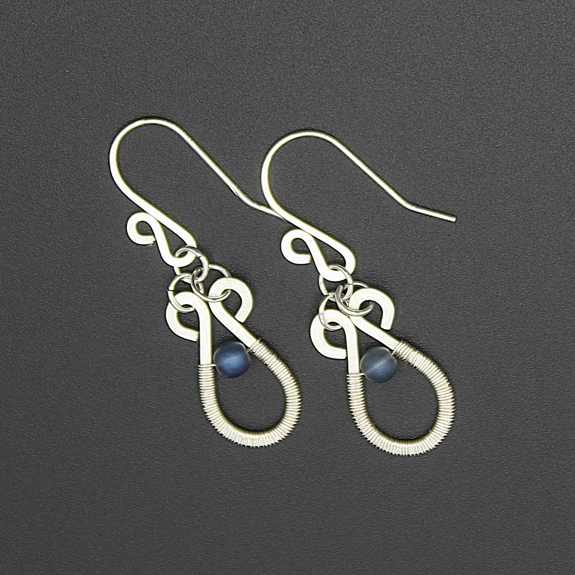 Hammered silver teardrop earrings with wire-wrapped blue bead accents on a gray background.