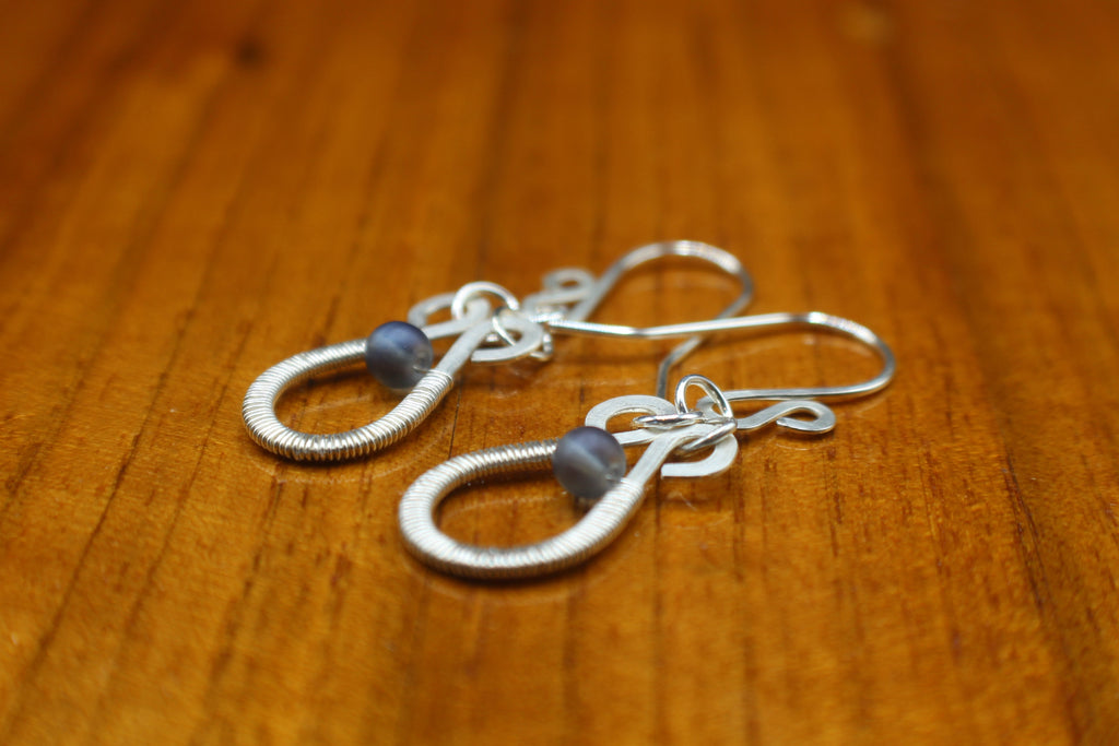 Hammered silver teardrop earrings with wire-wrapped blue bead accents on a wooden surface