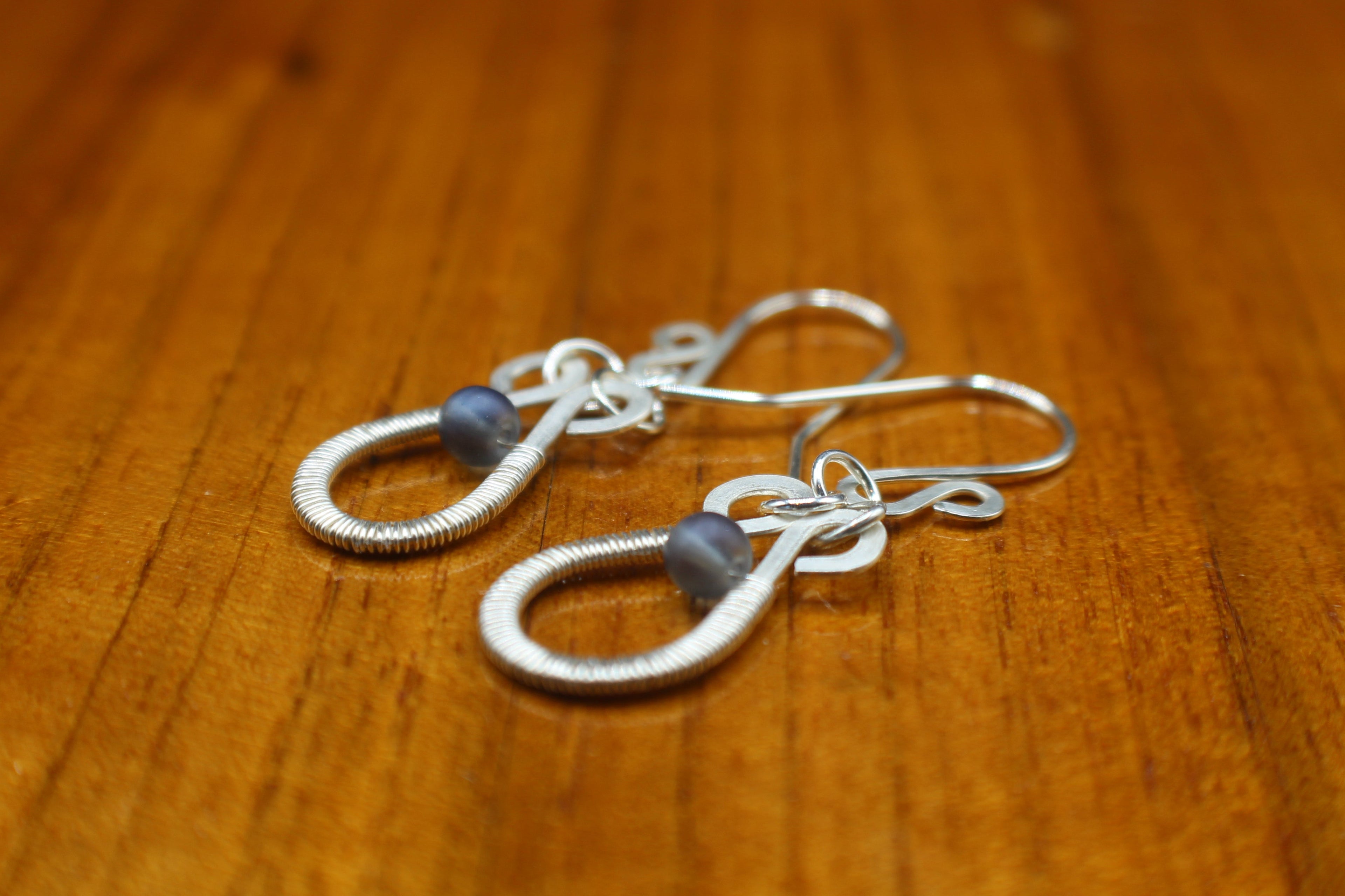 Hammered silver teardrop earrings with wire-wrapped blue bead accents on a wooden surface