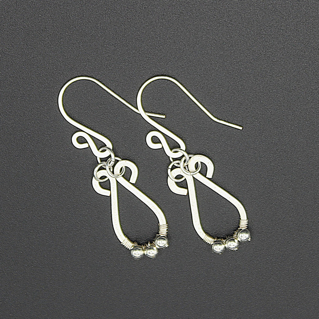 Hammered silver teardrop earrings with small silver bead accents on a gray background.