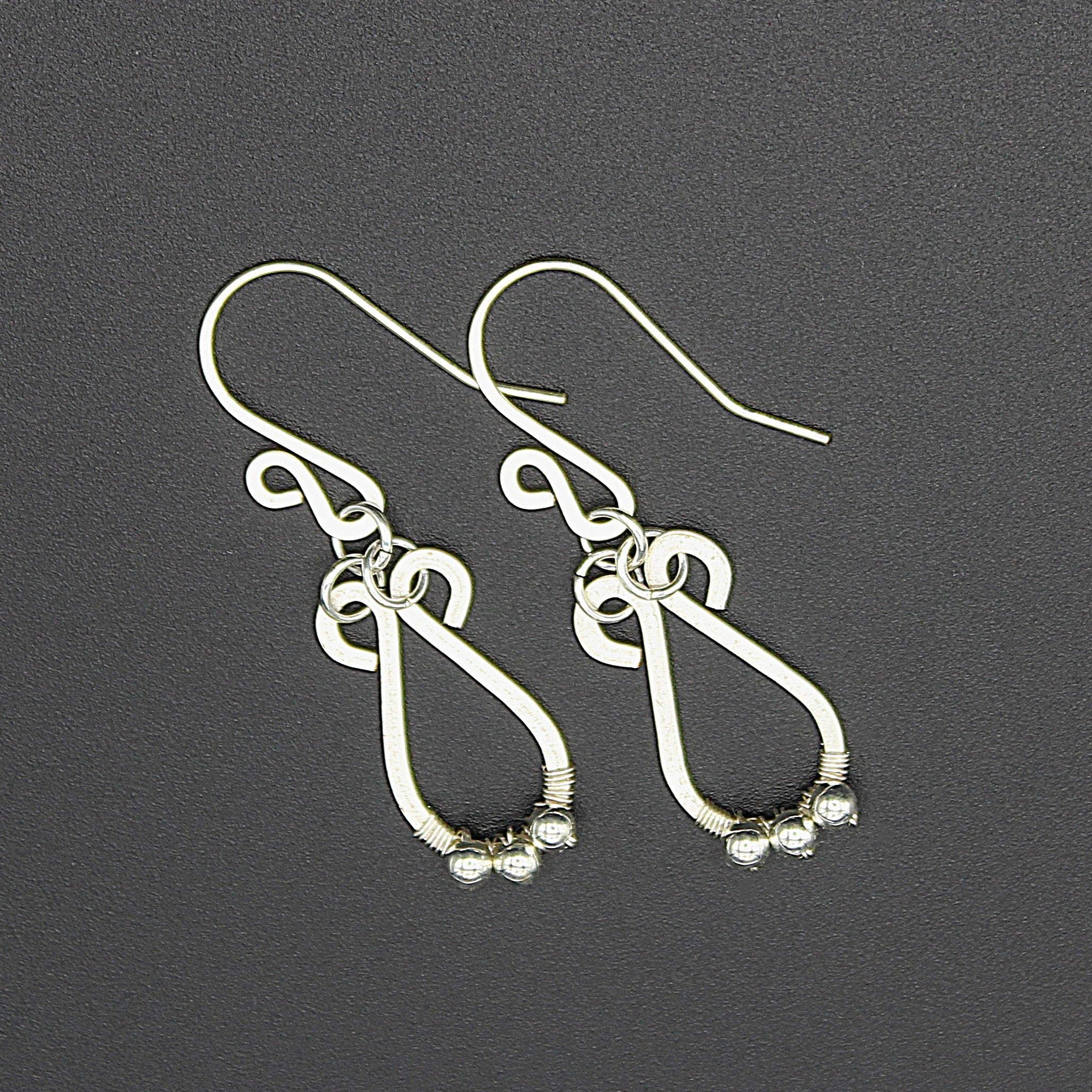 Hammered silver teardrop earrings with small silver bead accents on a gray background.