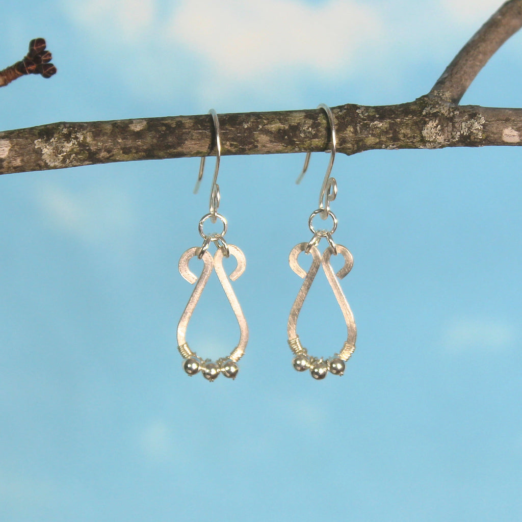 Hammered silver teardrop earrings with small silver bead accents hanging from a branch with a blue sky background