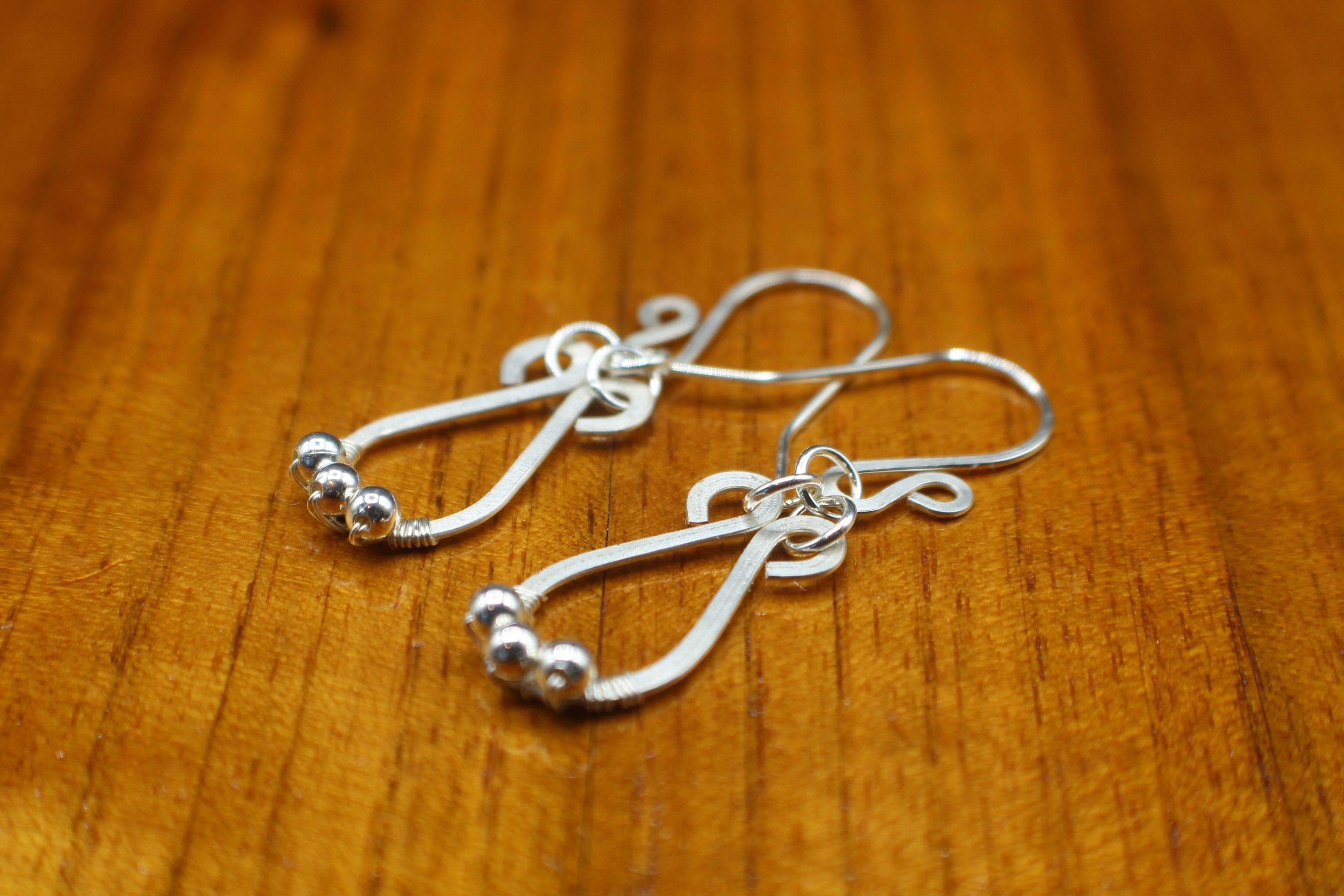 Hammered silver teardrop earrings with small silver bead accents on a wooden surface