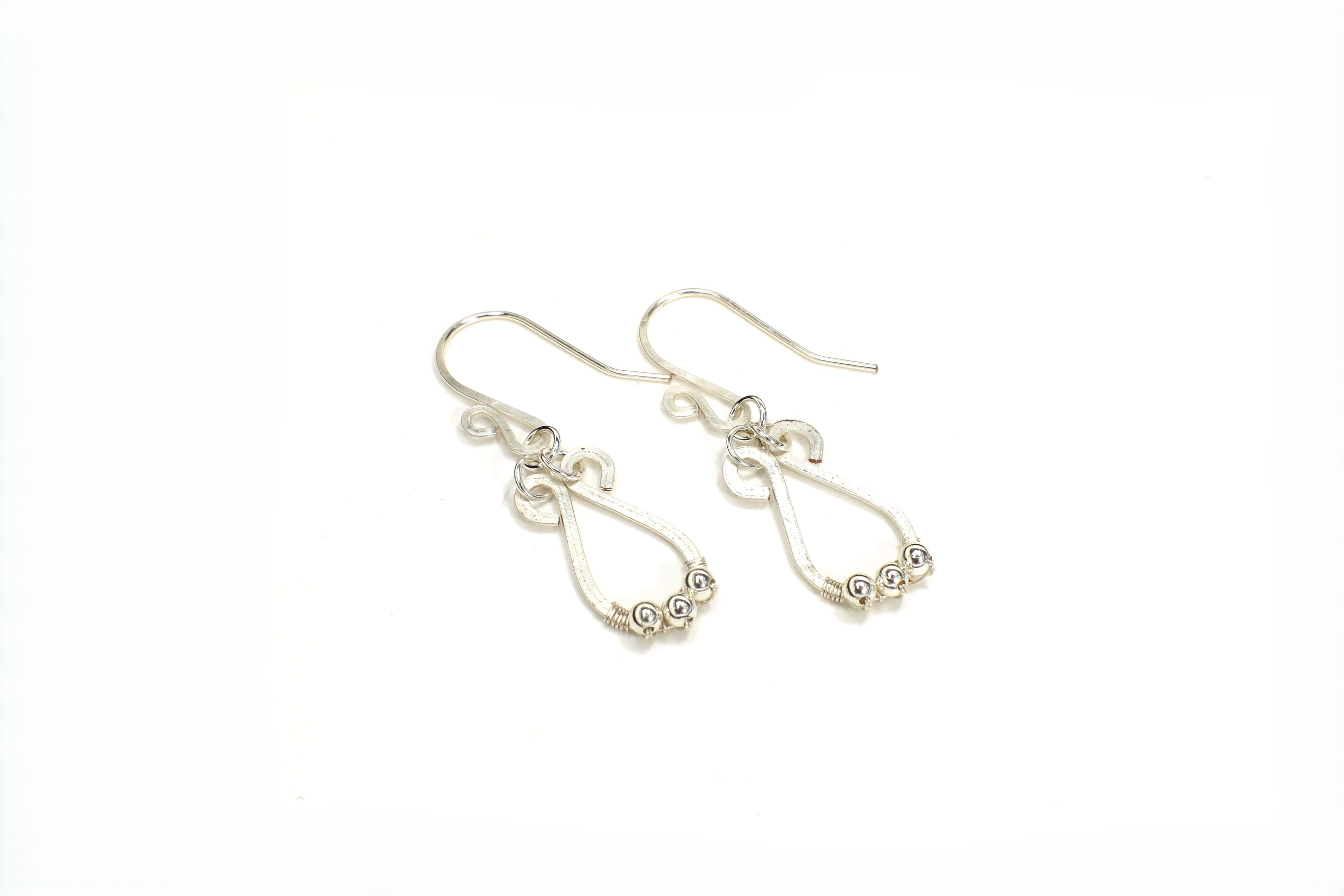 Hammered silver teardrop earrings with small silver bead accents on a white background