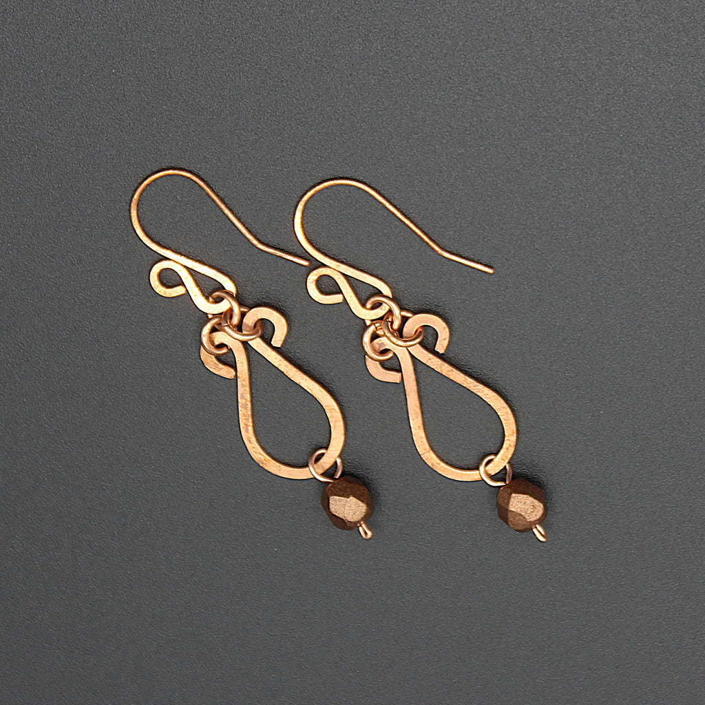 Hammered copper teardrop earrings with metallic finish faceted glass beads on a gray background.