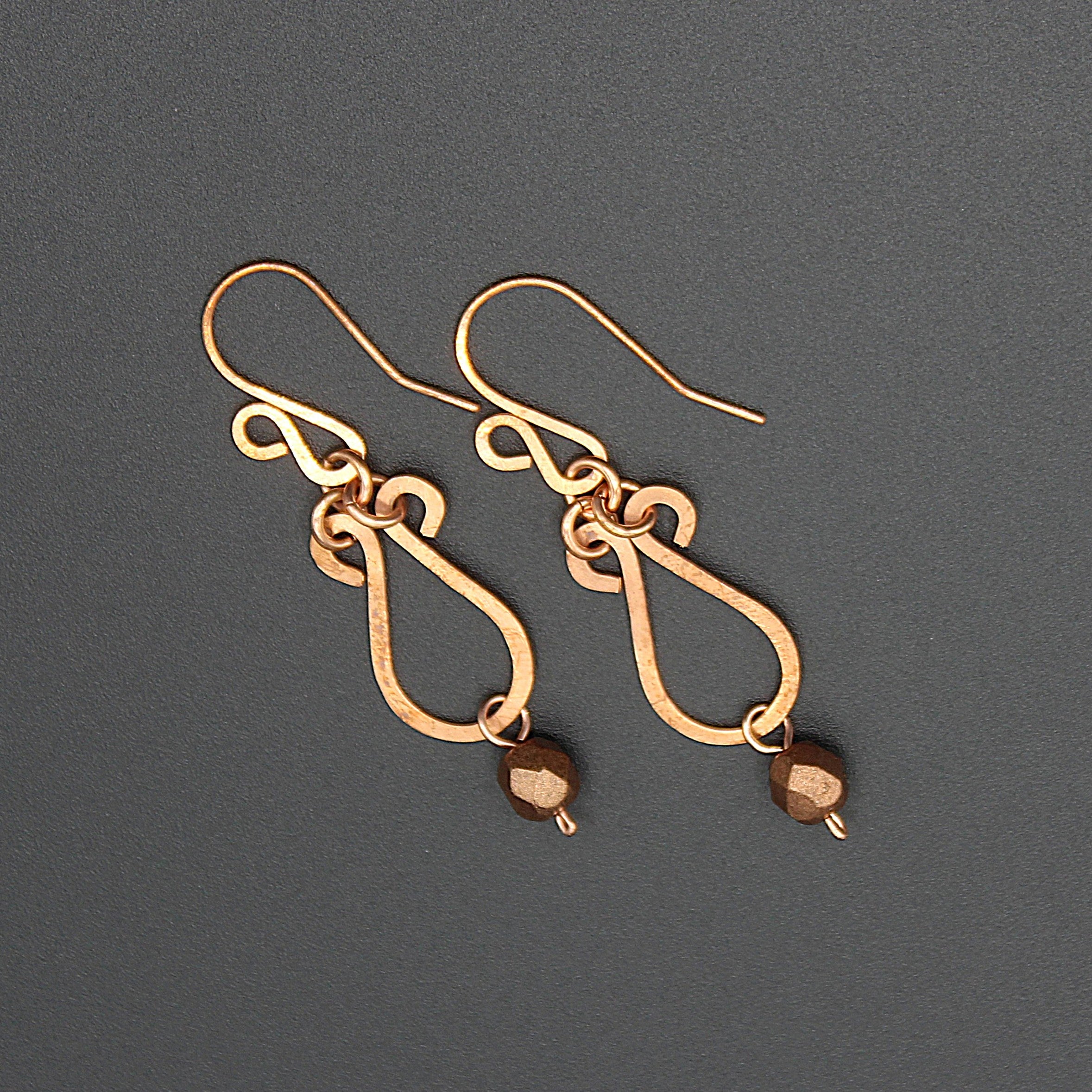 Hammered copper teardrop earrings with metallic finish faceted glass beads on a gray background.