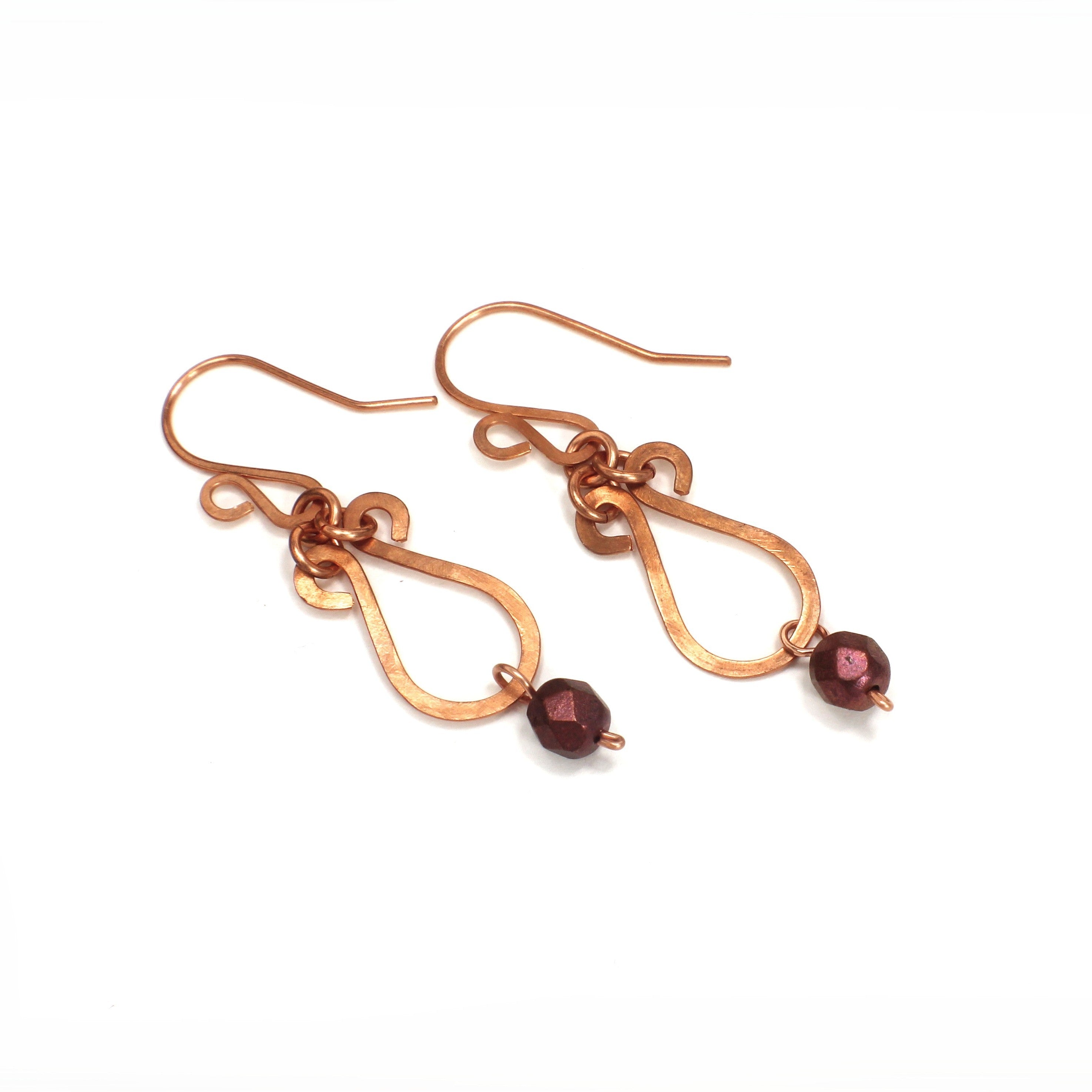 Hammered copper teardrop earrings with metallic finish, faceted glass beads on a white background