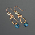 Hammered copper teardrop earrings with blue transparent bead drops on a gray background.