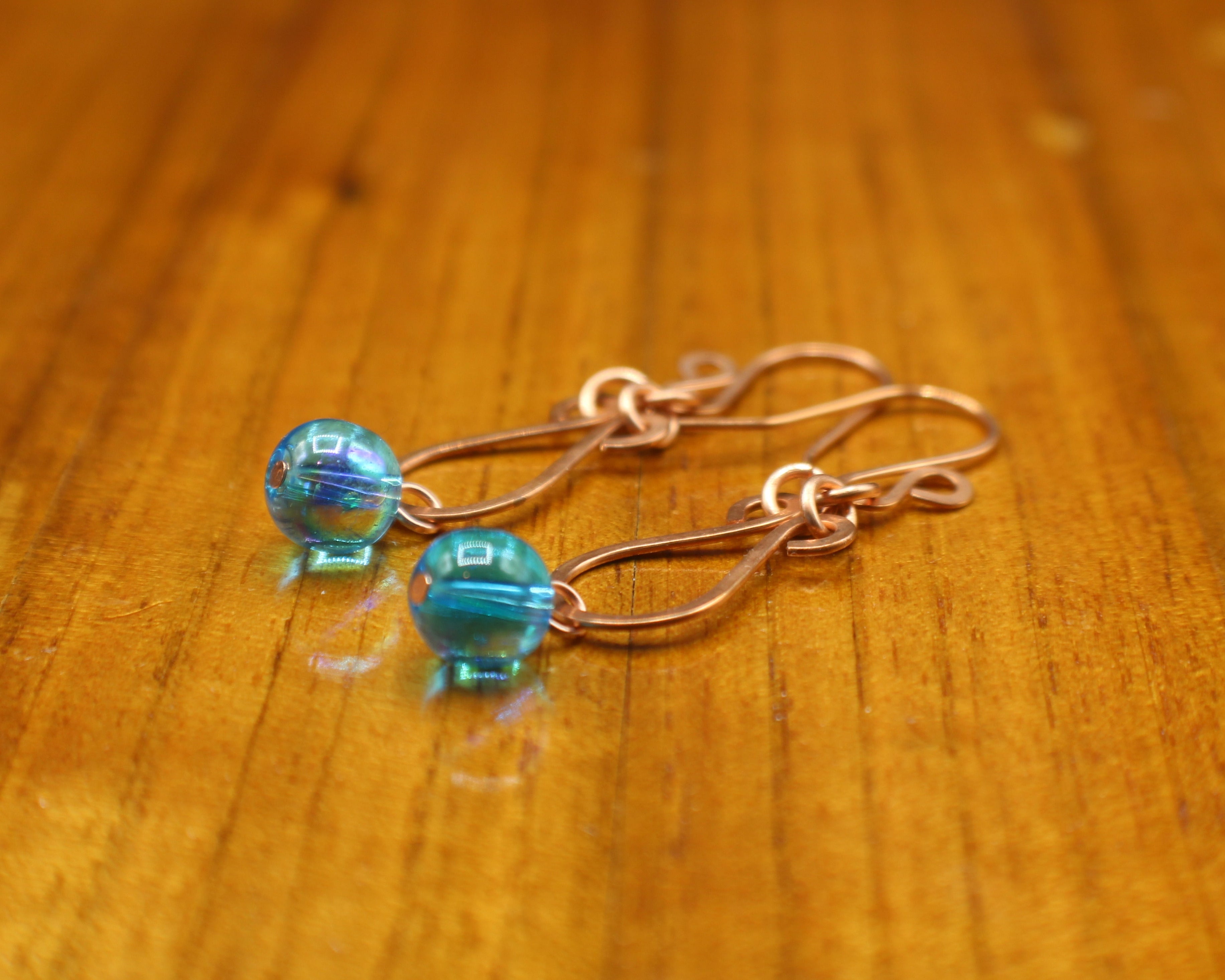 Hammered copper teardrop earrings with blue transparent bead drops on a wooden surface