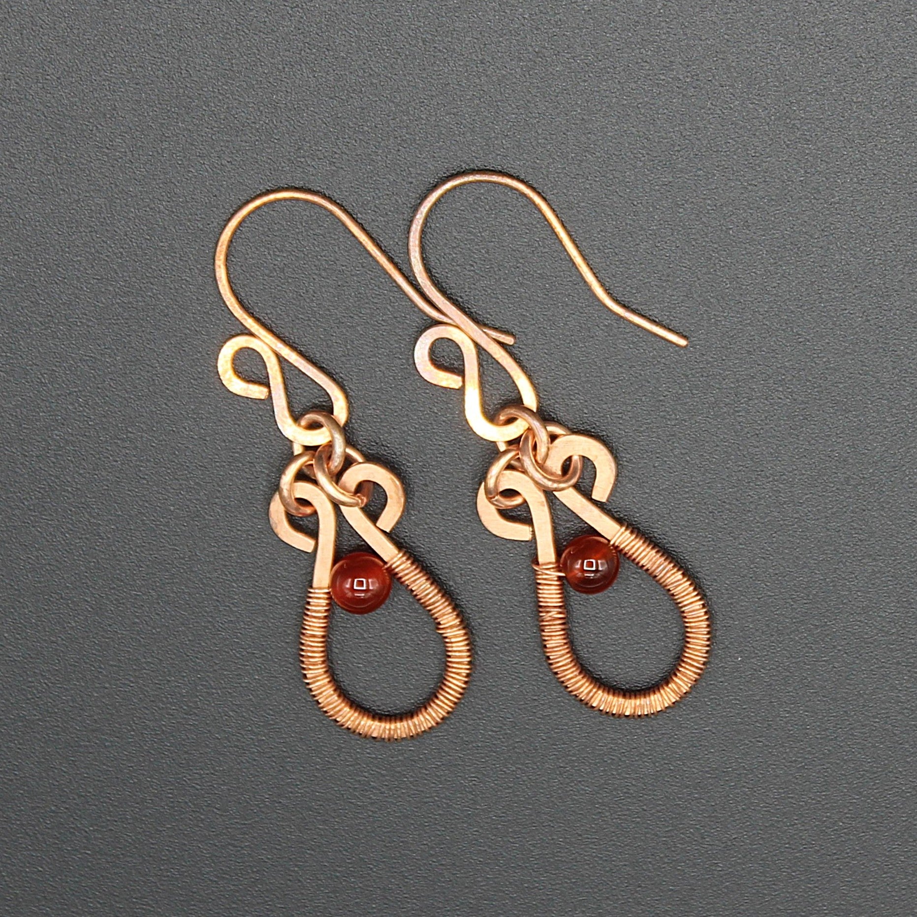 Flat wire copper teardrop earrings wire wrapped with carnelian bead accents on a gray background.