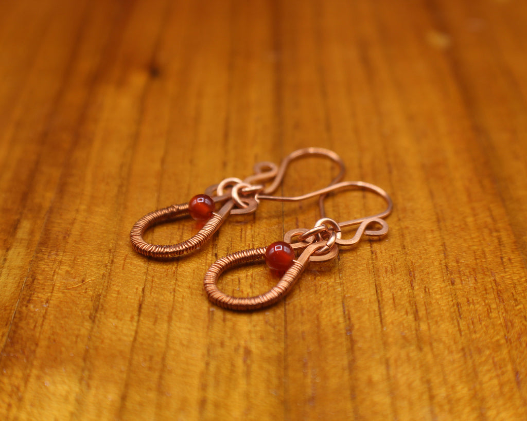 Flat copper teardrop earrings wire-wrapped with red carnelian bead accents  on a wooden surface