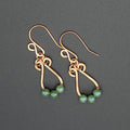 Hammered copper teardrop earrings with small green bead accents on a gray background.