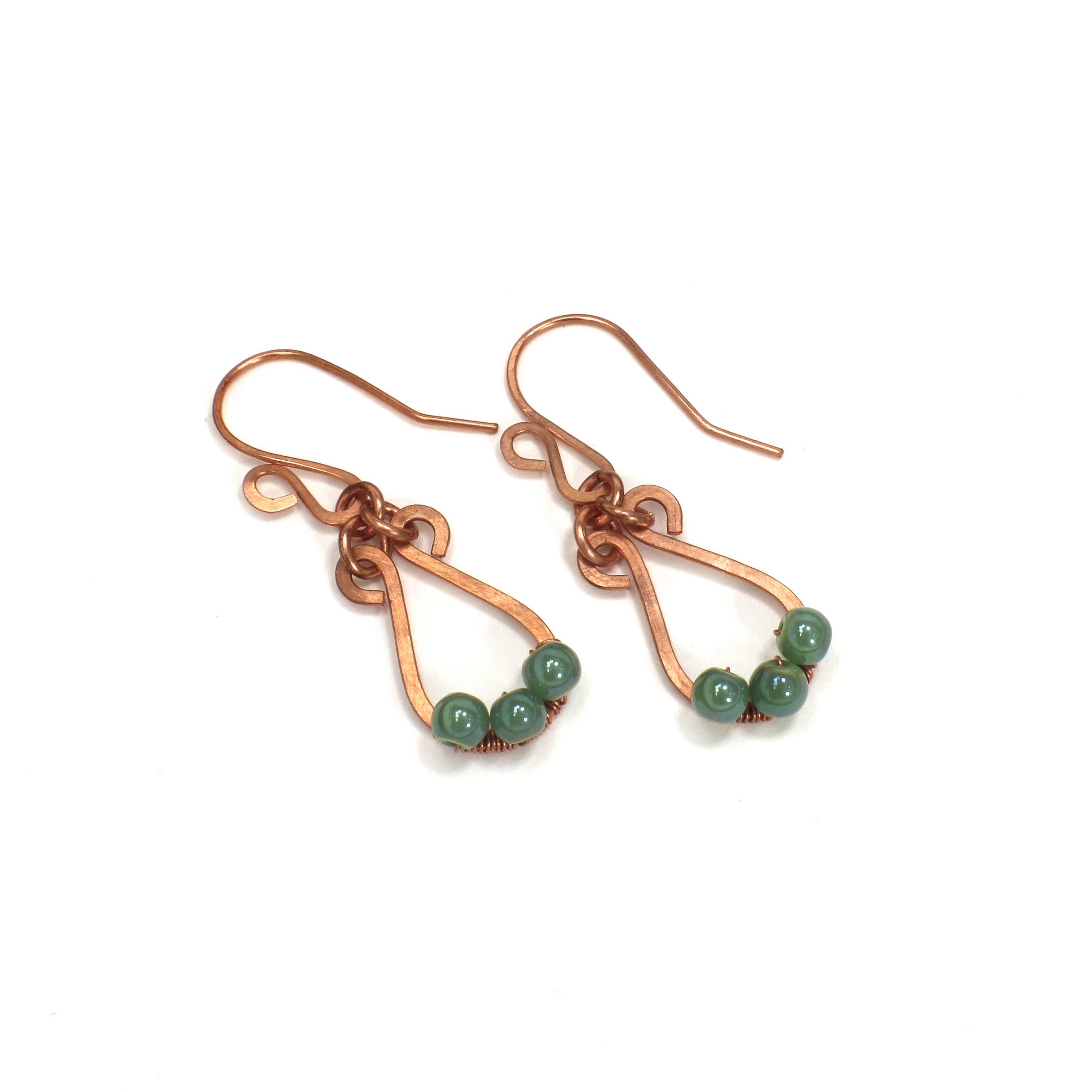 Hammered copper teardrop earrings with small green bead accents on a white background