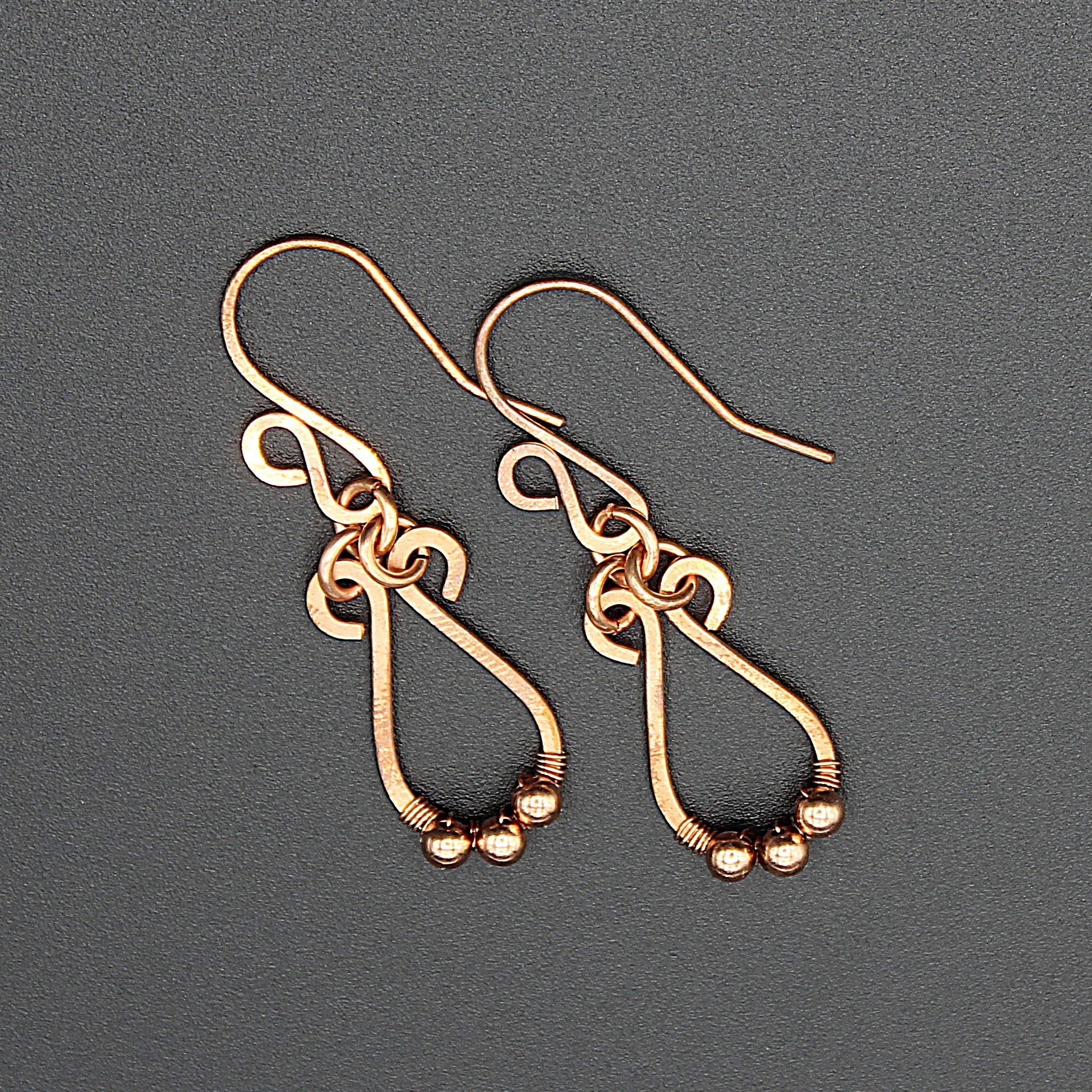 Hammered copper teardrop earrings with tiny wrapped beads on a gray background