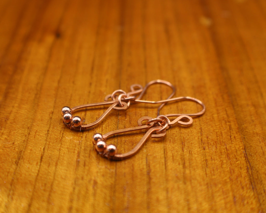 Hammered copper teardrop earrings with tiny wrapped beads on a gray background on a wooden surface