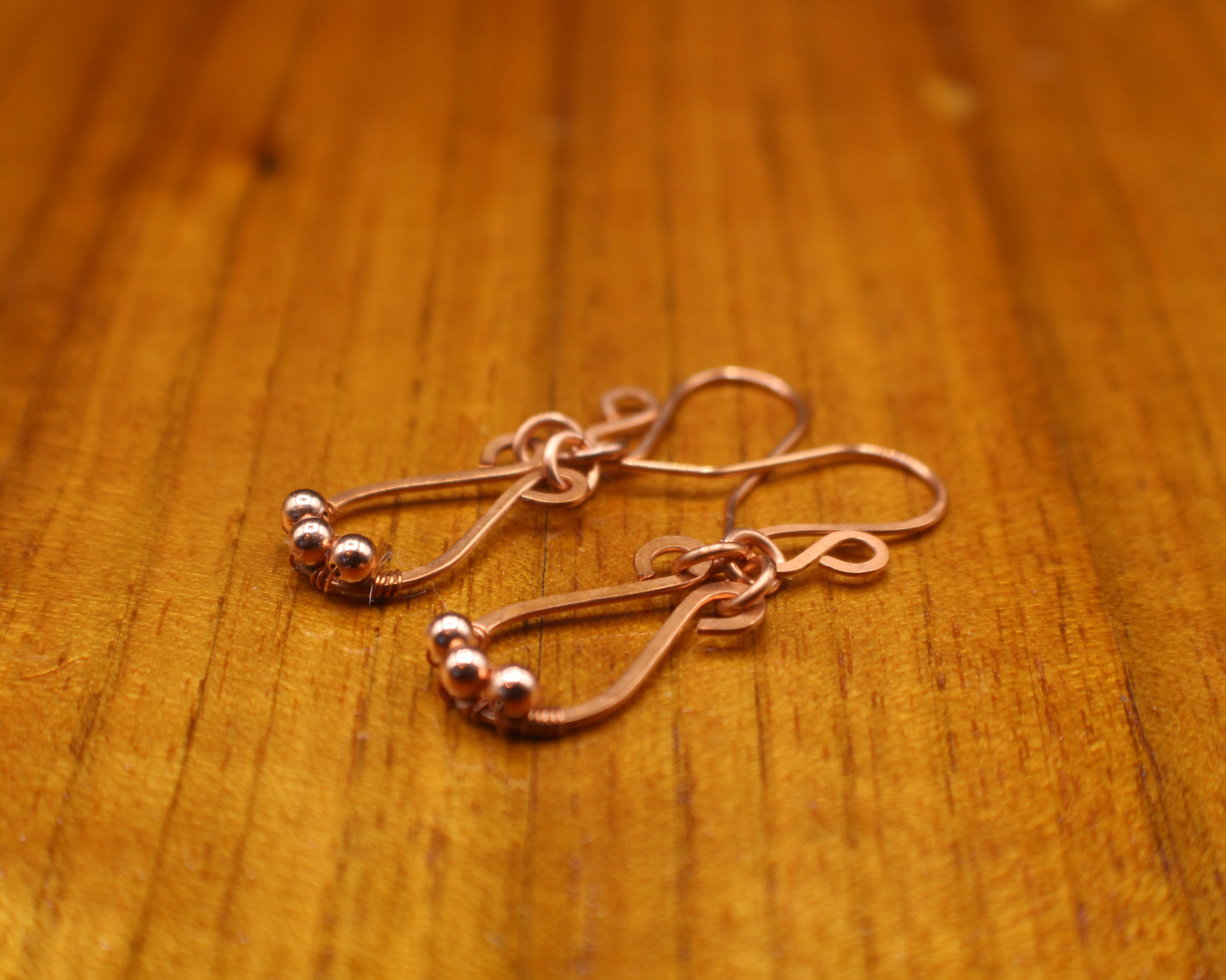 Hammered copper teardrop earrings with tiny wrapped beads on a gray background on a wooden surface