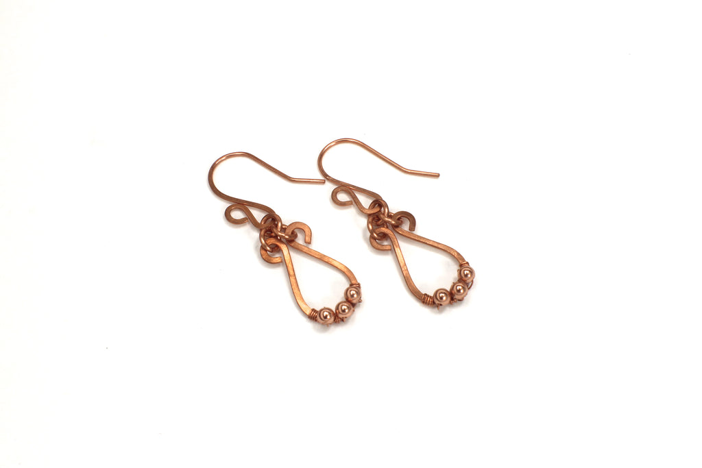 Hammered copper teardrop earrings with tiny wrapped beads on a gray background on a white background