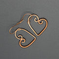 Pair of copper wire heart-shaped earrings wrapped with thin wire on half, on a gray background.