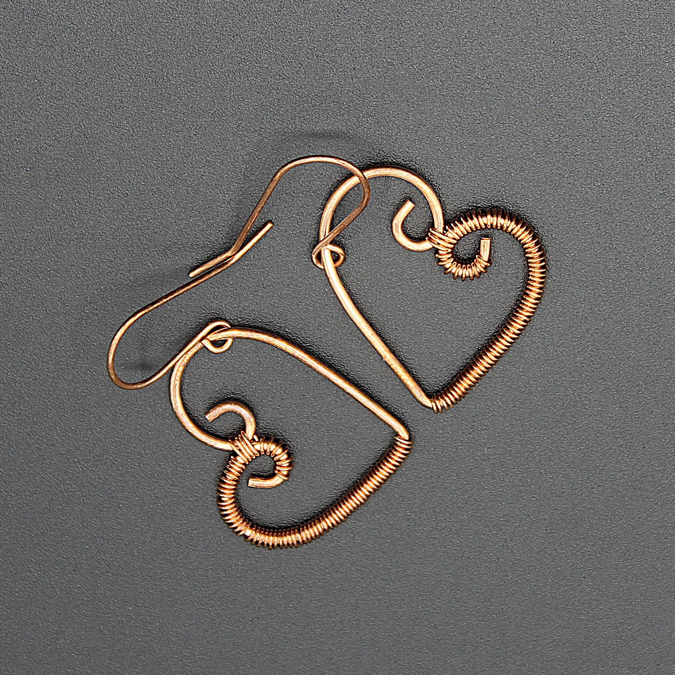 Pair of copper wire heart-shaped earrings wrapped with thin wire on half, on a gray background.