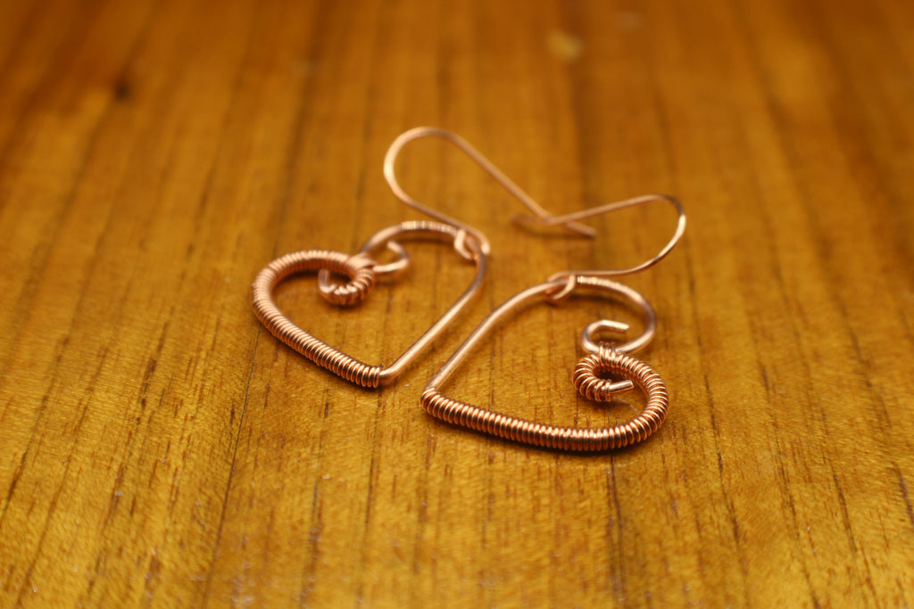 Heart-shaped copper wire earrings on a wooden surface