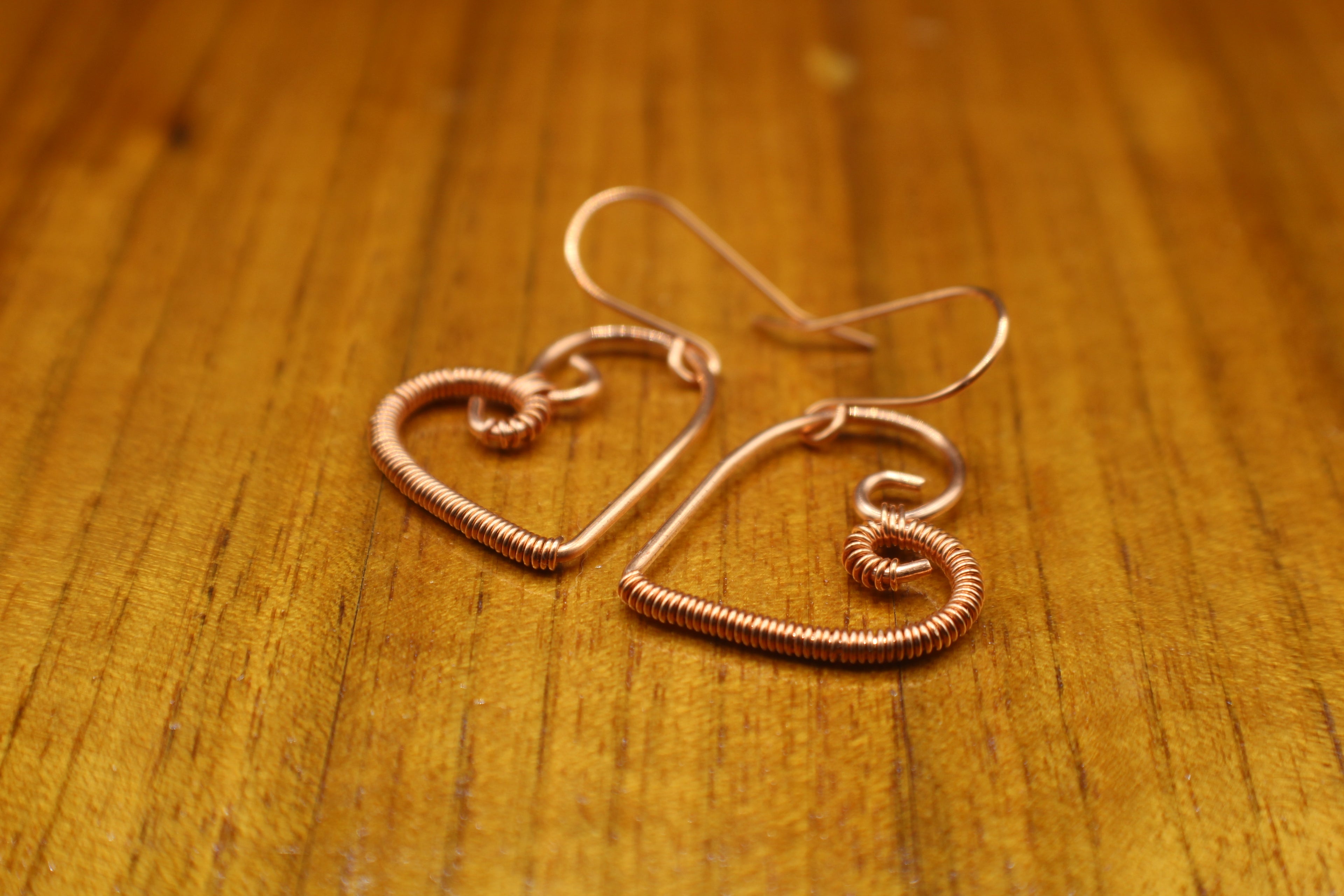 Heart-shaped copper wire earrings on a wooden surface