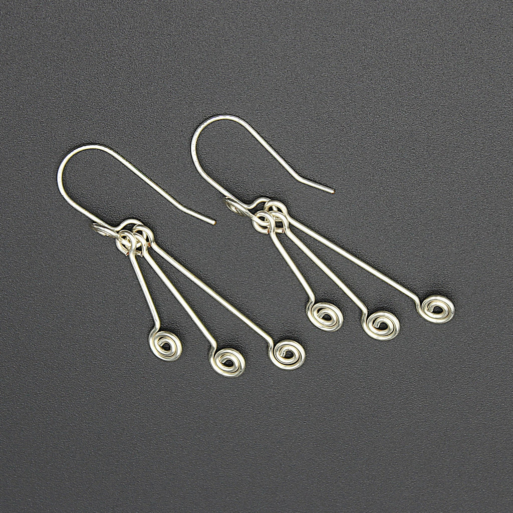 Silver wire earrings with hanging triple spirals on a gray background