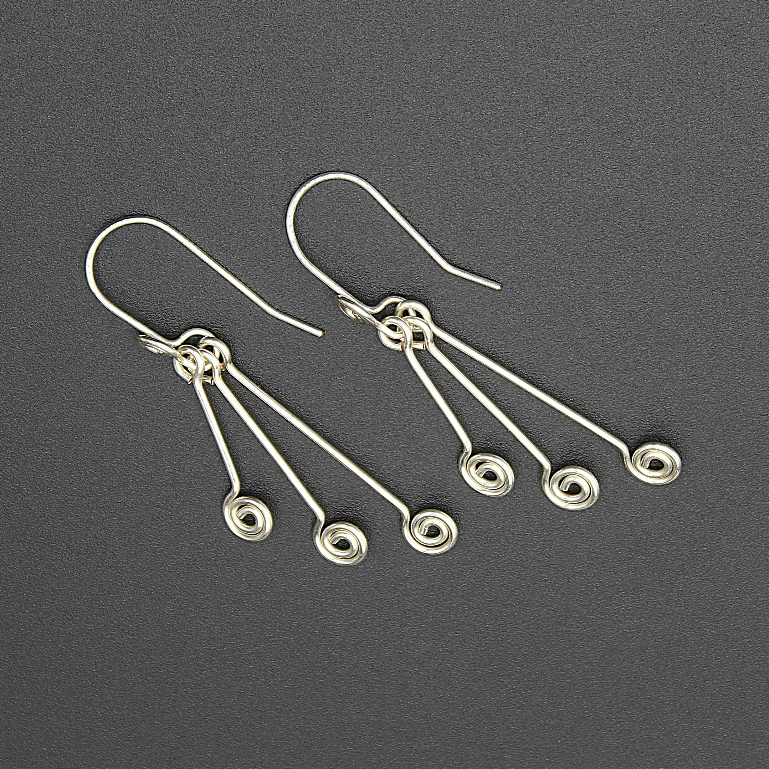 Silver wire earrings with hanging triple spirals on a gray background